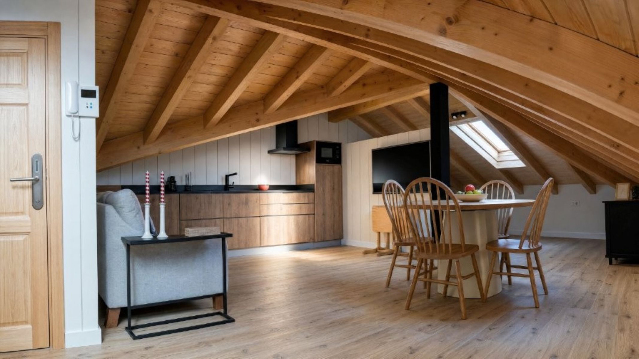 A loft-style room with a wooden ceiling, a dining area with a table and chairs, and a kitchenette.