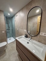 Un baño con ducha, inodoro y tocador con espejo.