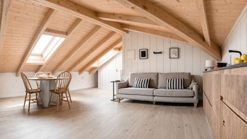 Una habitación con techos altos y un techo de madera inclinado, una mesa de comedor con sillas, un sofá y una pequeña mesita auxiliar.
