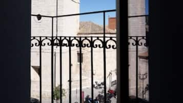 Un balcón con baranda de hierro forjado que da a una calle con motocicletas estacionadas y un edificio con torre.