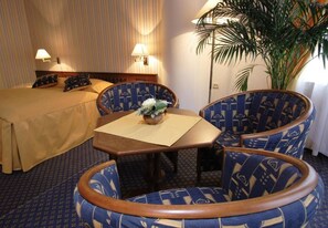 Una habitación de hotel con cama, dos sillones, una mesita con un florero y una planta en maceta.