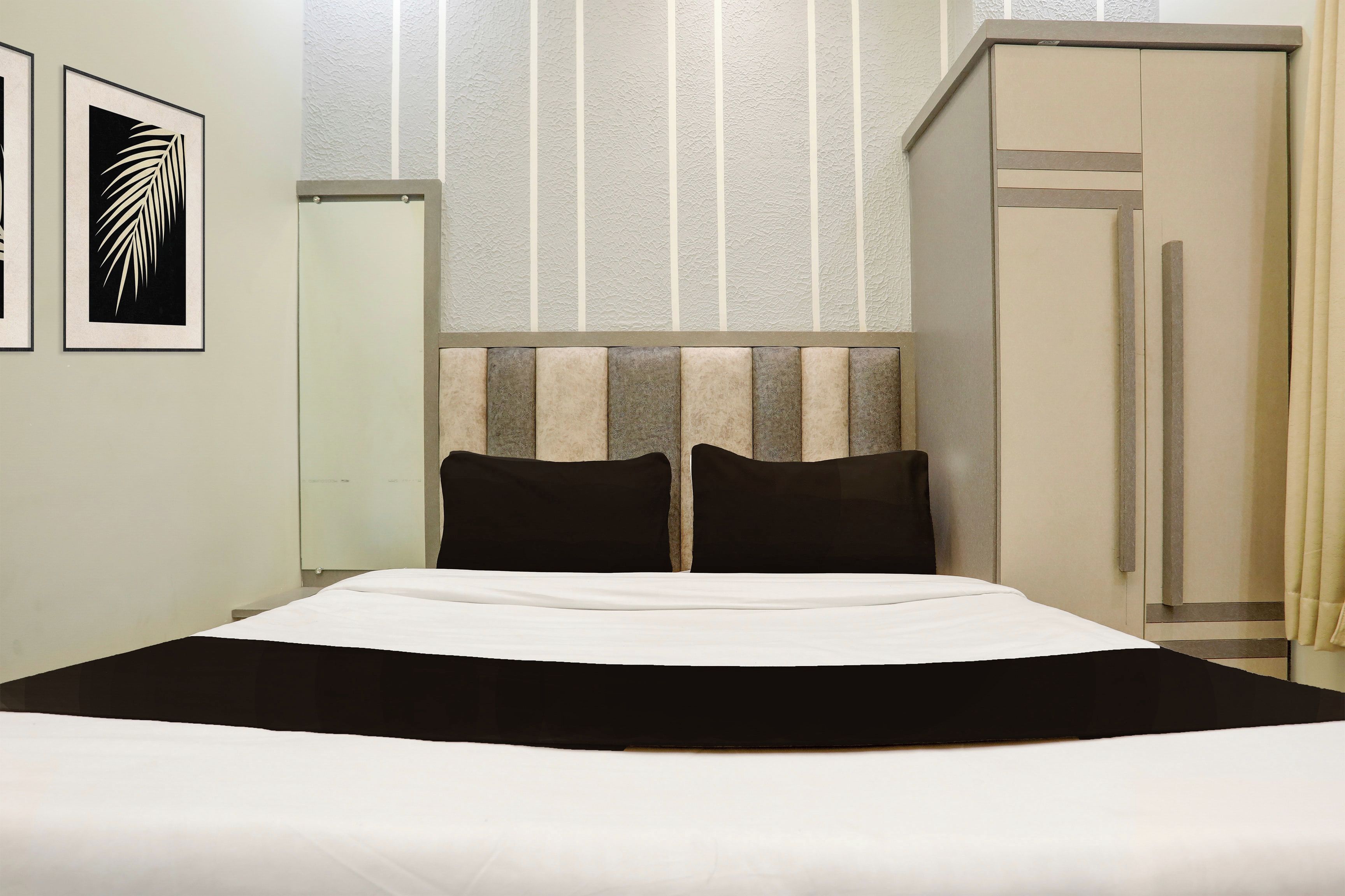 A hotel room with a bed, a wardrobe, and two framed pictures on the wall.
