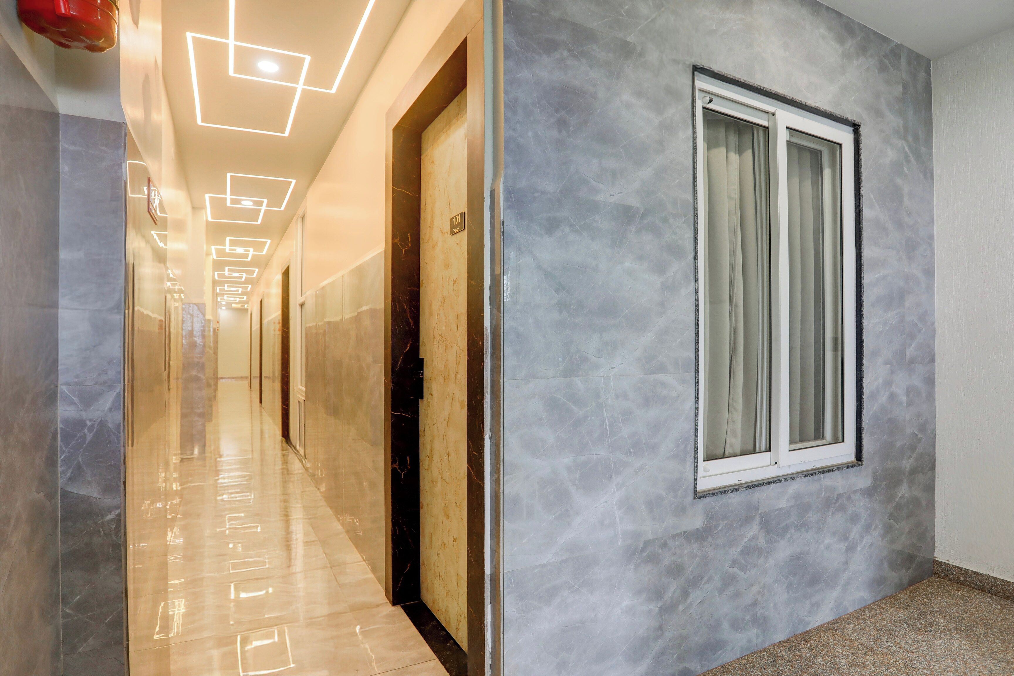 A hallway with a marble floor, a door with a number plate, and a window with curtains.
