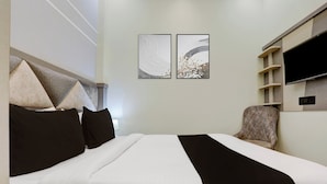 A hotel room with a bed, a chair, a television, and two wall-mounted artworks. - Super Hotel O Maharshi Valmiki Airport  (Faizabad)