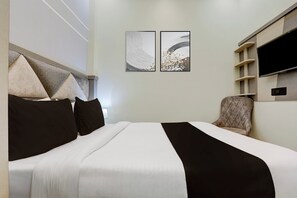 Hotellihuone, jossa on sänky, tuoli, televisio ja kaksi seinälle ripustettua taideteosta.