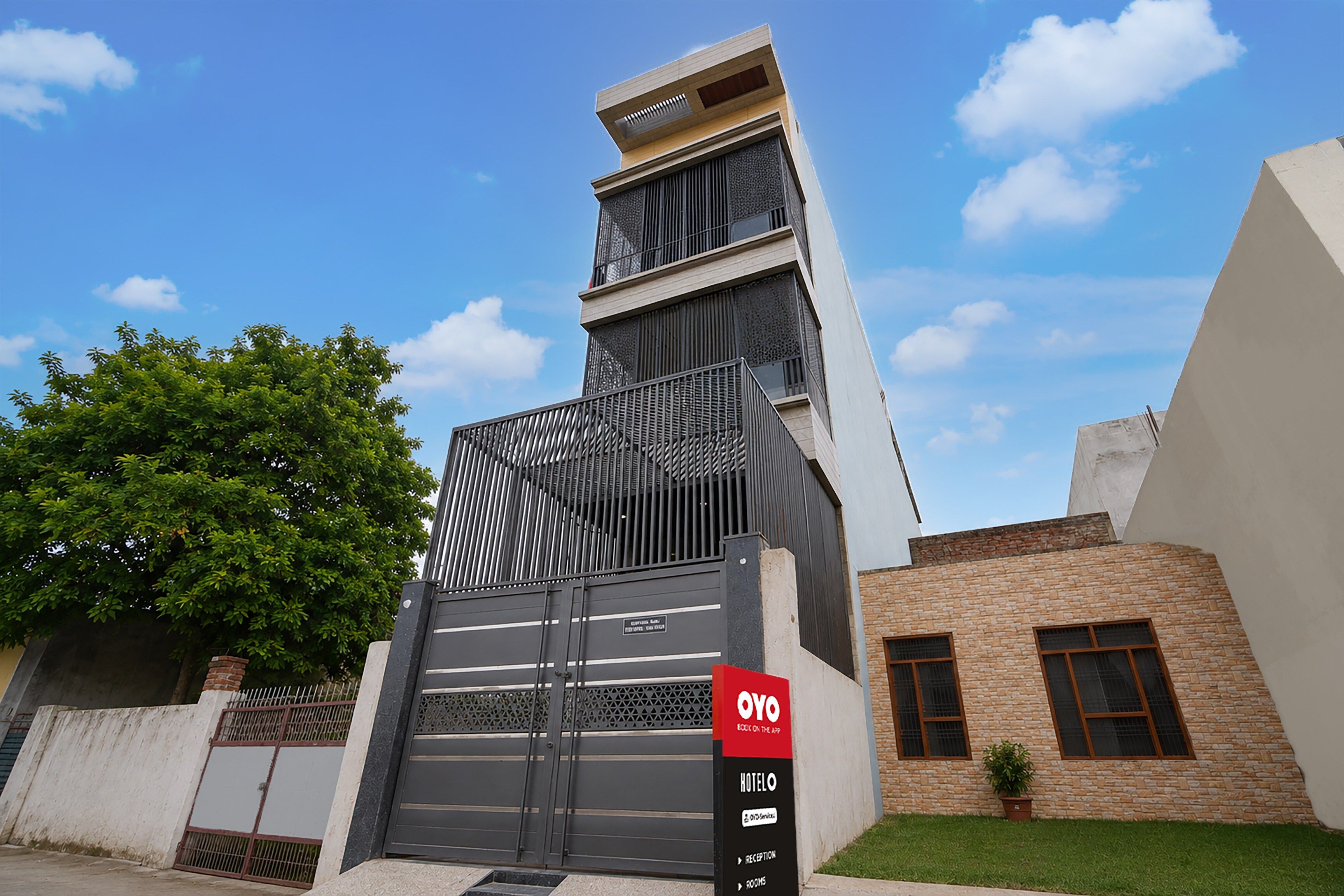 A modern hotel entrance with a gated driveway, a reception desk, and a staircase leading to the entrance.