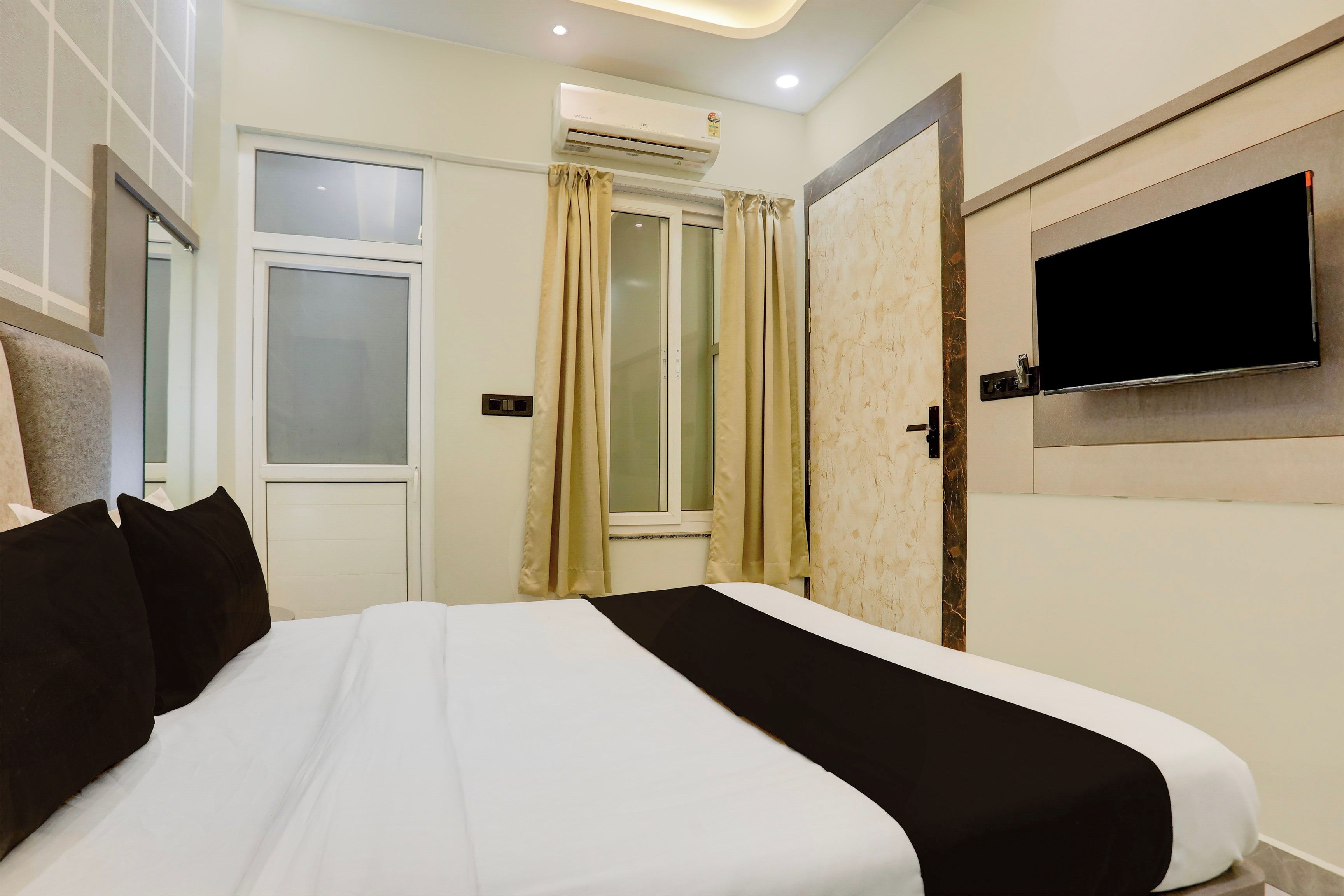 A hotel room with a bed, a TV mounted on the wall, and an air conditioning unit.