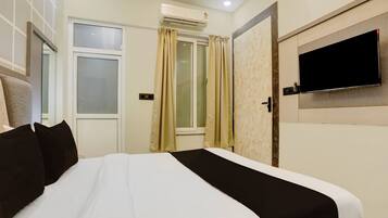 A hotel room with a bed, a TV mounted on the wall, and an air conditioning unit.