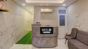 A hotel reception area with a marble reception desk, a grey sofa, and a wall-mounted air conditioner. - Super Hotel O Maharshi Valmiki Airport  (Faizabad)