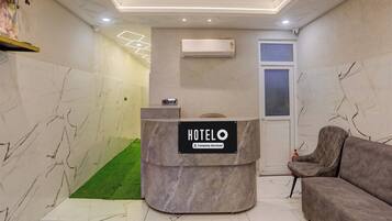 A hotel reception area with a marble reception desk, a grey sofa, and a wall-mounted air conditioner.