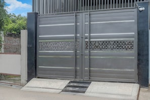 Um portão de metal com câmera de segurança, cerca de metal e parede de concreto.