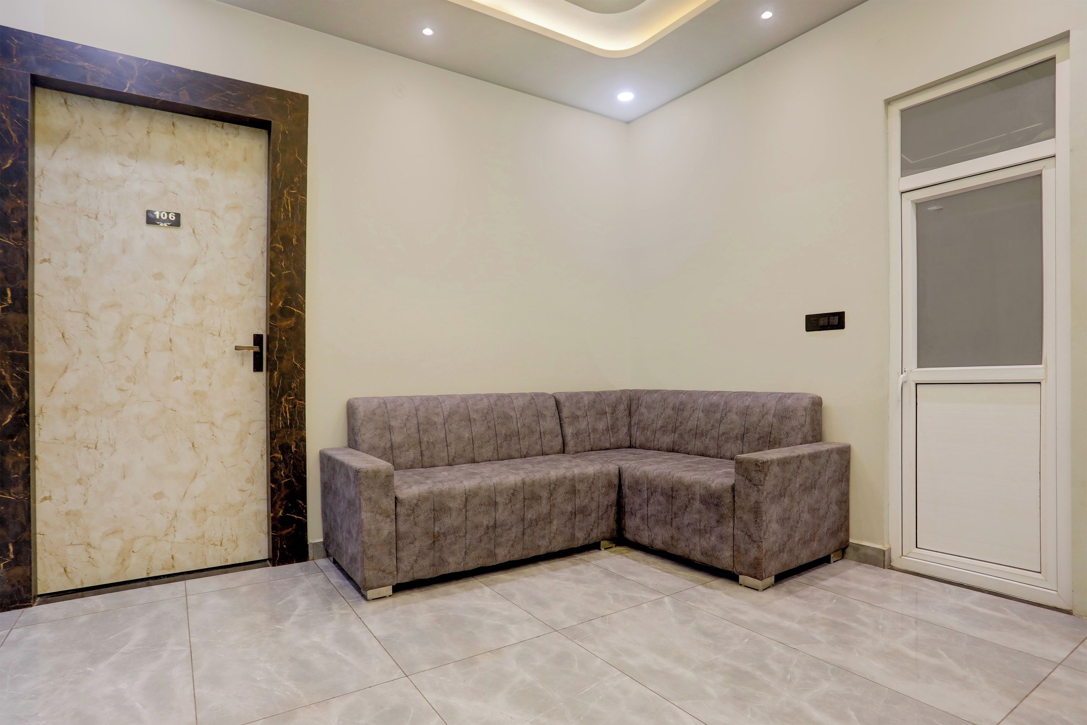 A room with a marble door, a grey sectional sofa, and a white door with a frosted glass panel.