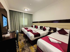 Habitación de hotel con tres camas, un escritorio con teléfono y una televisión.