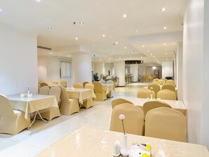 Uma sala de jantar espaçosa com várias mesas e cadeiras, dispostas em um ambiente moderno e bem iluminado.