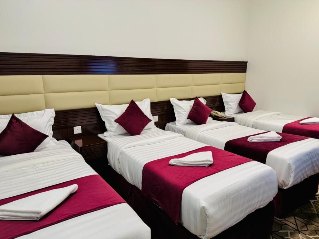 A hotel room with four beds arranged in a row, each with white bedding and red accents.