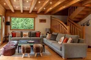 A cozy living room with a sofa set, ottomans, a coffee table, and a large window with a view of greenery. - Stylish Morzine chalet, centrally located with hot tub (Morzine)