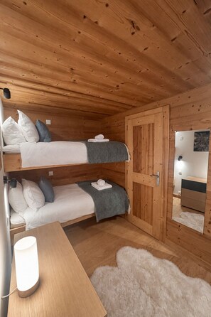 A wooden cabin room with bunk beds, a desk, a mirror, and a fluffy rug. - Stylish Morzine chalet, centrally located with hot tub (Morzine)