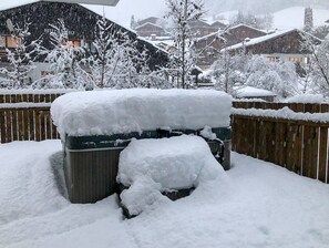 Área externa coberta de neve, com cerca de madeira, uma lixeira e edifícios ao fundo.