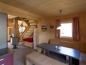 Ein Holzinnenraum mit Essbereich, einer Bank, einem Tisch, einer Treppe und einem Fenster mit Vorhängen.