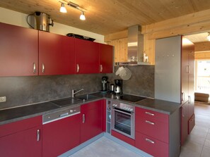 Eine moderne Küche mit roten Schränken, Edelstahlgeräten und einer Holzbalkendecke.