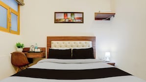 Habitación de hotel con cama, mesita de noche, lámpara, estante en la pared, ventana con marco de madera y una pequeña planta en maceta.