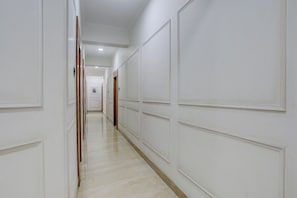 Um corredor com paredes brancas e piso de madeira, que leva a um quarto com porta.