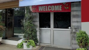 Entrada de un edificio con un letrero que dice 'WELCOME', puertas de vidrio y plantas en macetas.