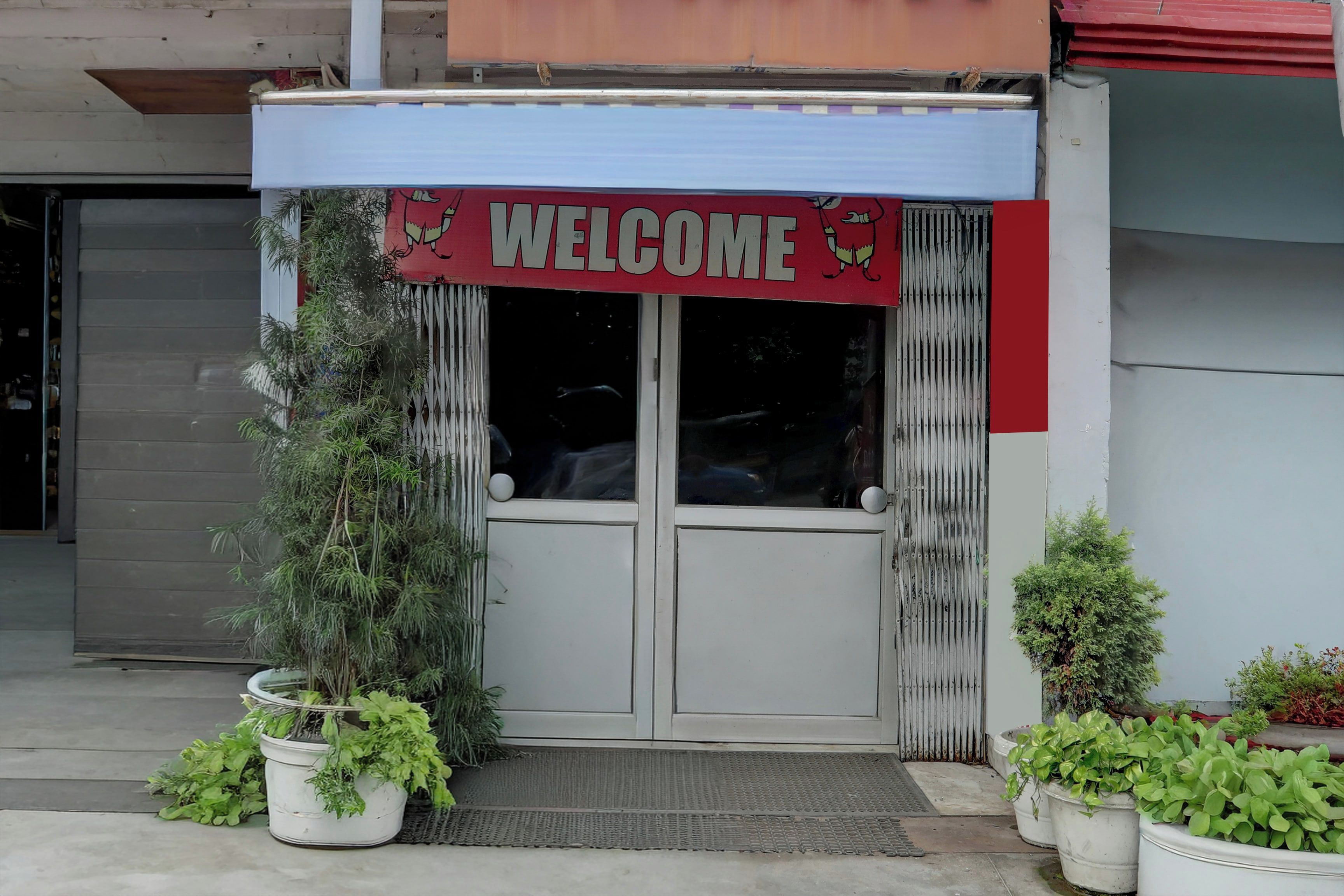 Entrada de un edificio con un letrero que dice 'WELCOME', una reja de metal y plantas en macetas.