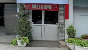 Entrada de un edificio con un letrero que dice 'WELCOME', una reja de metal y plantas en macetas.