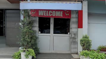 Entrada de un edificio con un letrero que dice 'WELCOME', una reja de metal y plantas en macetas.