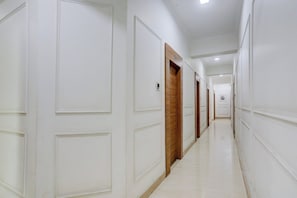 A hallway with white walls, wooden doors, and a tiled floor. - Collection O Haldwani Railway Junction (Haldwani)