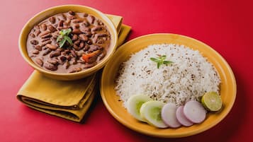 A bowl of curry with beans and a plate of rice with cucumber slices and a lime wedge.