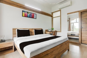 A modern bedroom with a wooden bed, a bedside table, a nightstand, a mirror, and a colorful artwork on the wall. - Collection O Haldwani Railway Junction (Haldwani)