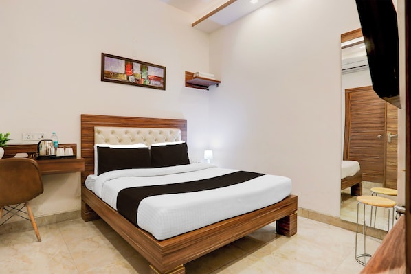 Quarto de hotel com cama de madeira, mesa de cabeceira, cadeira, escrivaninha, espelho e obra de arte pendurada na parede.