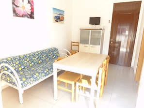 A room with a sofa, a dining table, chairs, a cabinet, and a television. - Apartment With Terrace in Village With Pools (San Michele al Tagliamento)