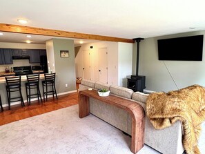 A living room with a sofa, a coffee table, a fireplace, and a kitchen area with bar stools. - SlopeTown Retreat - Big Sky Meadow (Big Sky)