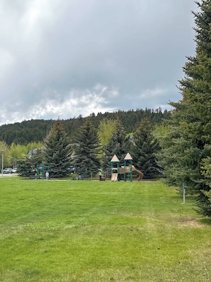 A park with a playground, a grassy field, and a forested hill in the background. - SlopeTown Retreat - Big Sky Meadow (Big Sky)