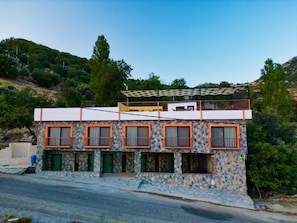A two-story building with a stone facade, multiple windows with orange frames, and a balcony on the upper floor. - ELM PANSİYON (Fethiye)