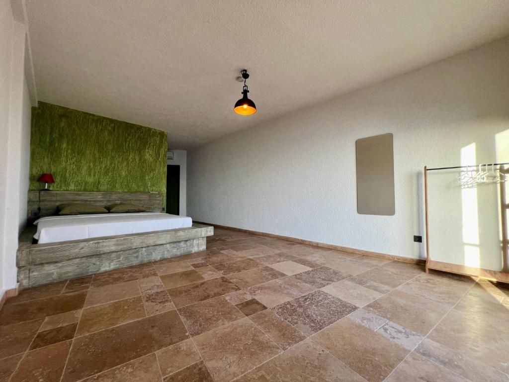 A room with a bed, a green textured wall, a hanging light fixture, and a glass door.