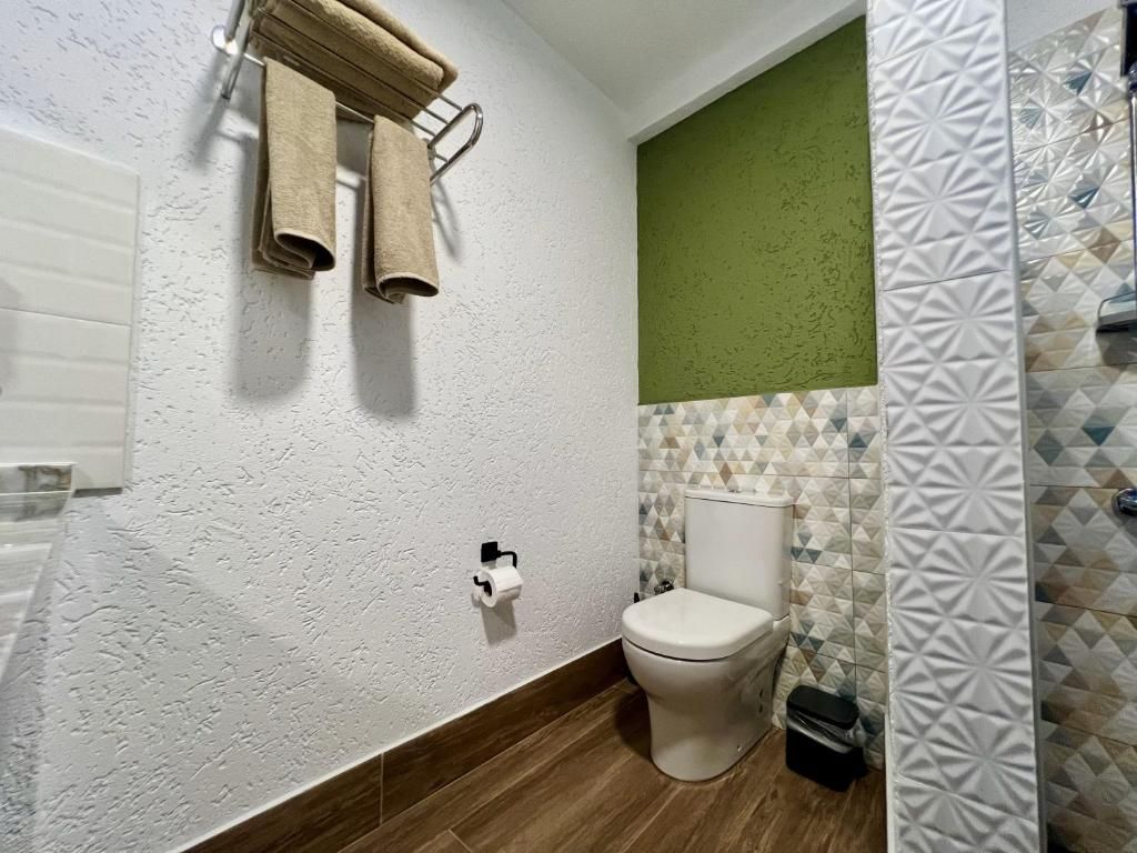 A bathroom with a toilet, a towel rack, a trash bin, and patterned tiles.