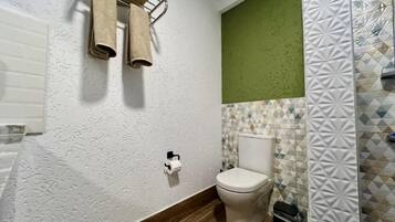 A bathroom with a toilet, a towel rack, a trash bin, and patterned tiles.