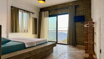 A bedroom with a bed, a wooden bench, a hanging light fixture, a balcony with a view, and a brick wall.
