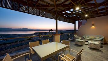 Una terraza con una mesa y sillas, con vista a un paisaje que incluye una masa de agua y montañas.
