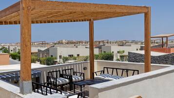 Una terraza en la azotea con una pérgola de madera, mobiliario exterior y suelo de piedra.