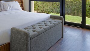 Quarto com cama, um banquinho e ventilador de teto.