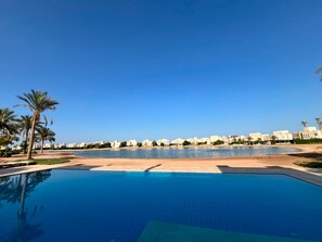 A swimming pool with a clear view of the beach and buildings in the background. - Vesta - Luxury APT - 2BR - Joubal (El Gouna)