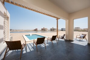 Ein überdachter Außenbereich mit Pool, Liegestühlen und Blick auf Strand und Gebäude.