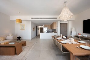 Ein modernes Wohnzimmer mit einem Holzesstisch, gedeckt für vier Personen, einer Küche im Hintergrund und einer Pendelleuchte.