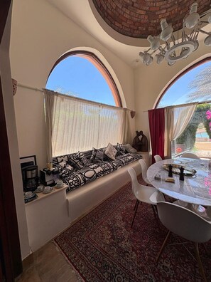 A room with a built-in bench, a dining table, and a view through arched windows. - Vesta - Luxury Twin House - 3BR - Nubia (El Gouna)