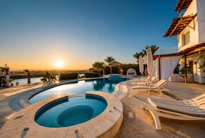 Ein Poolbereich mit Blick auf den Sonnenuntergang, Liegestühle und ein Gebäude mit einem Ziegeldach.